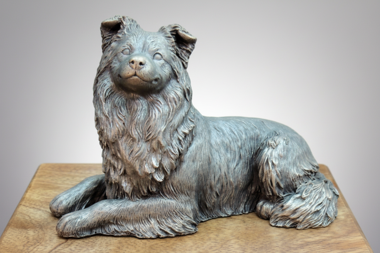 Bronze sculpture of a Border dog on a wooden stand with a gray background