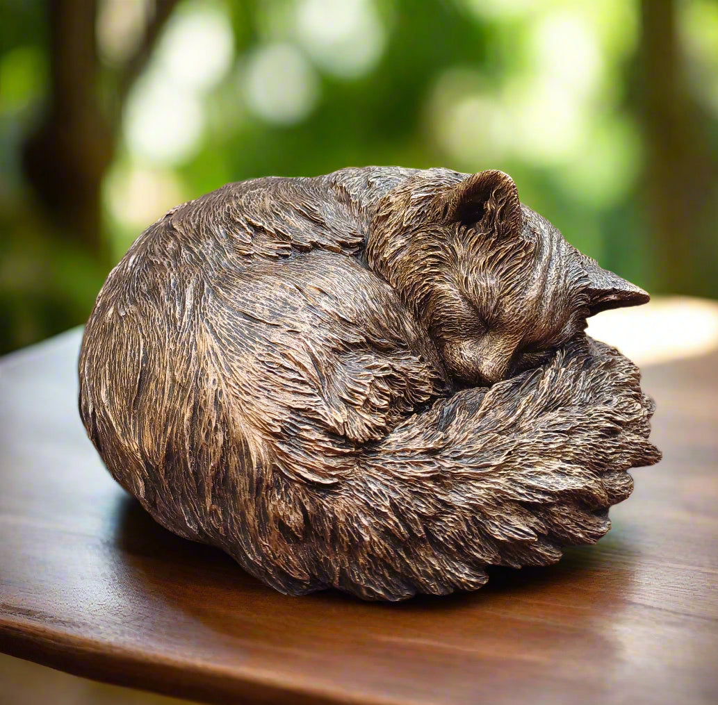 Sleeping cat sculpture curled up on a wooden surface next to a glass door