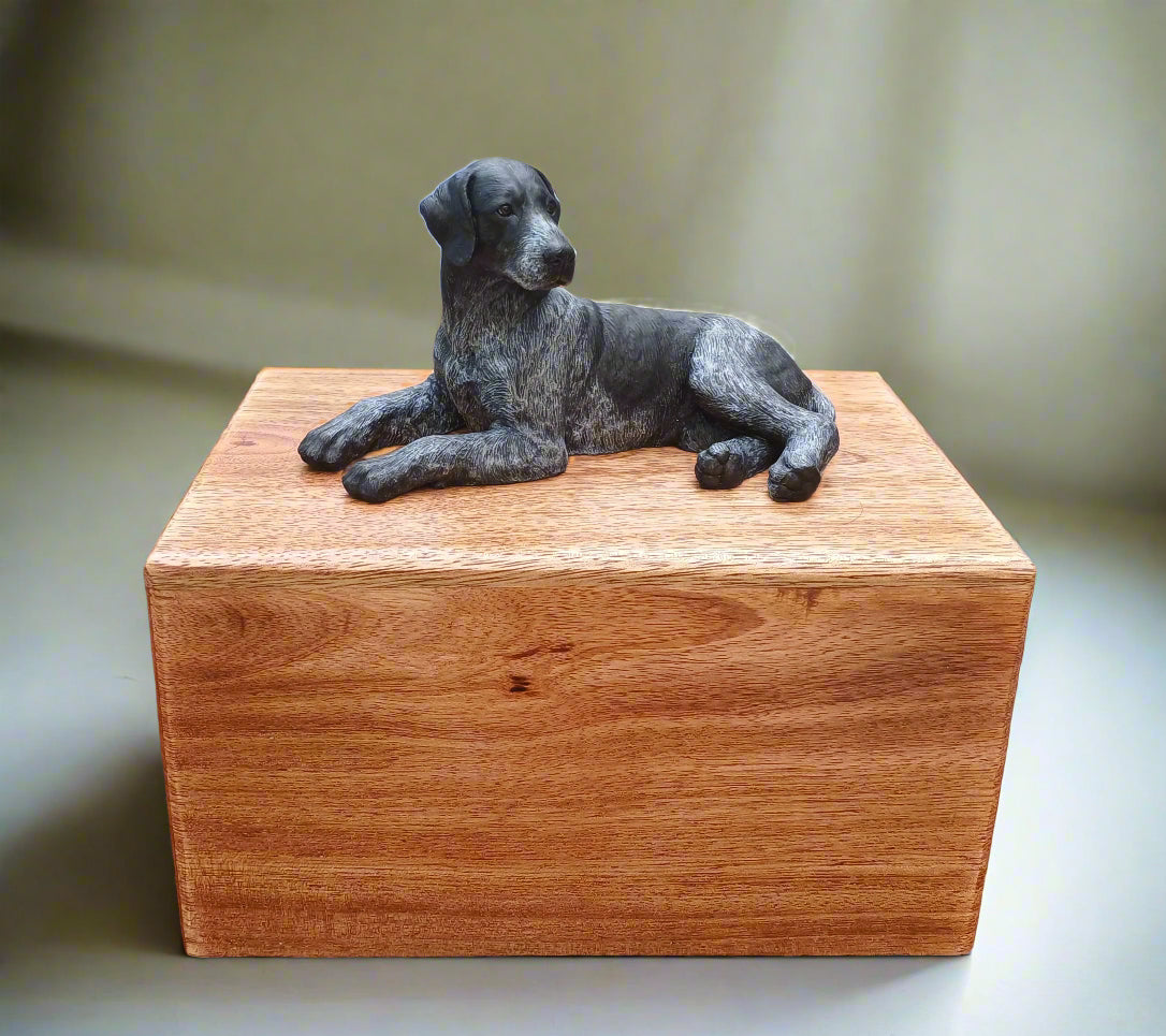 Wooden urn box with a dog figurine on top, placed on a wooden surface.