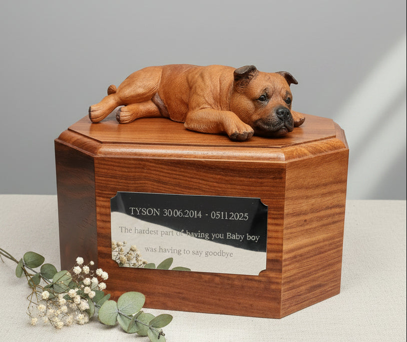 Wooden pet urn with a staffie dog figurine on top, placed on a wooden surface.