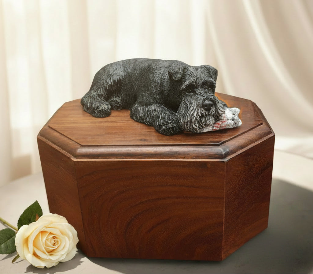 Wooden urn with a black schnauzer dog figurine on top, set against a blurred green outdoor background.